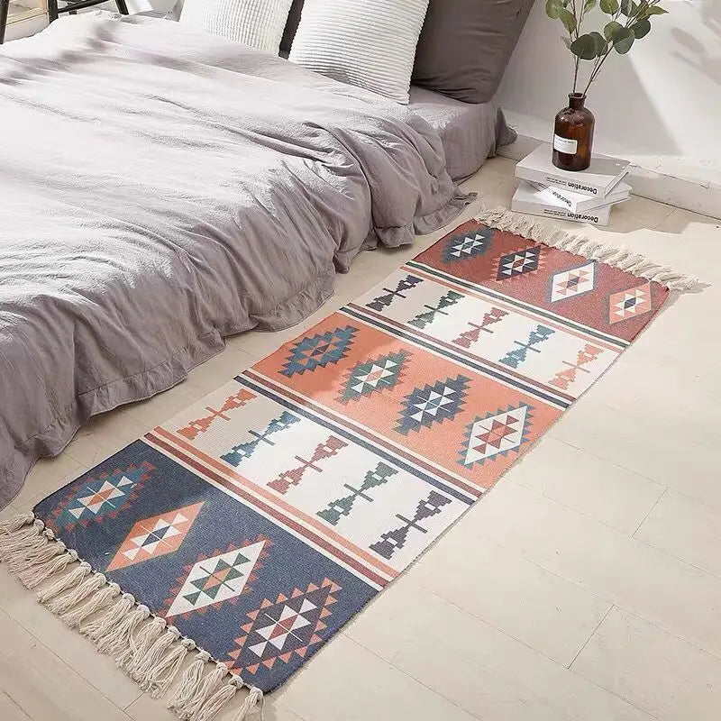 Tapis en coton et lin tissé main — motif berbère - Nesty, variante losanges orange, bleu et écru façon kilim, posée au pied d'un lit