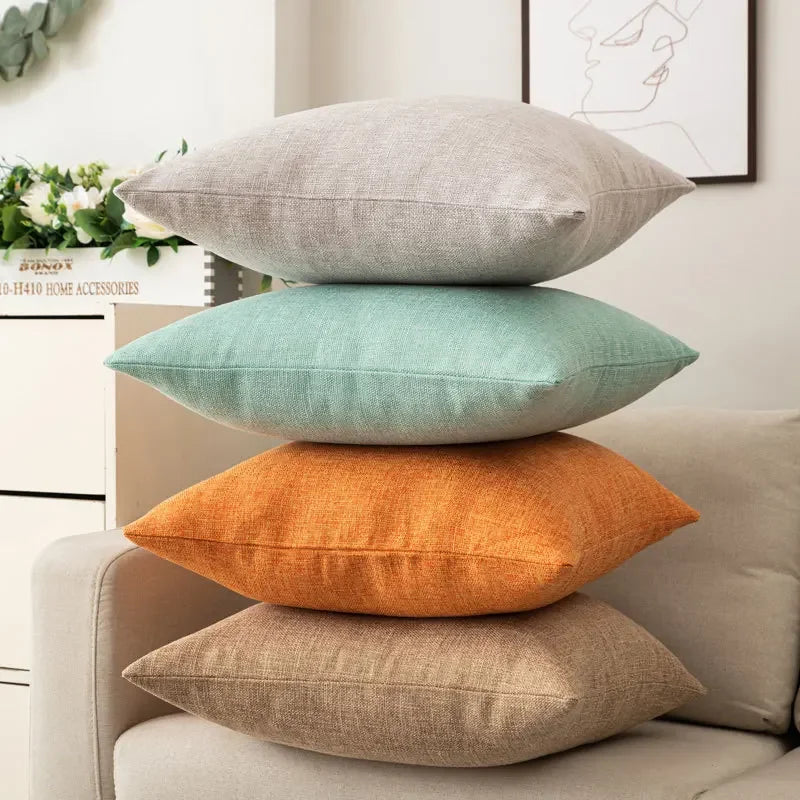 Coussin coloré avec garnissage inclus, style moderne et simple Nesty, quatre coussins unis empilés, coloris gris clair, vert menthe, orange et beige, sur accoudoir de canapé devant tableau abstrait