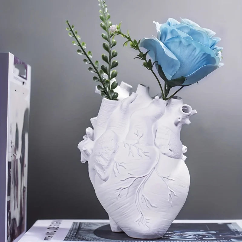 Vase en résine forme cœur, style nordique - Nesty - Coloris blanc avec rose bleue et brins verts, posé sur un magazine près d'un livre