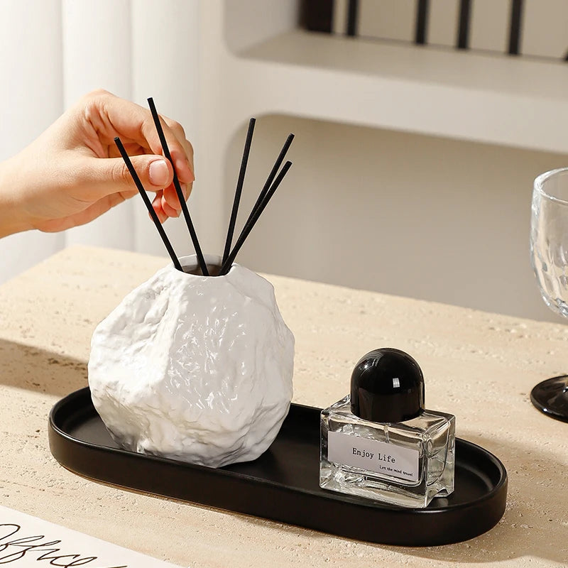 Diffuseur de parfum en céramique avec plateau Nesty - Vase texture roche blanche et bâtonnets, main ajustant les tiges, sur plateau noir ovale