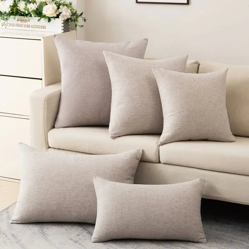 Coussin coloré avec garnissage inclus, style moderne et simple Nesty, cinq coussins unis beige clair, carrés et rectangulaires, posés sur canapé et au sol près d'une console à fleurs
