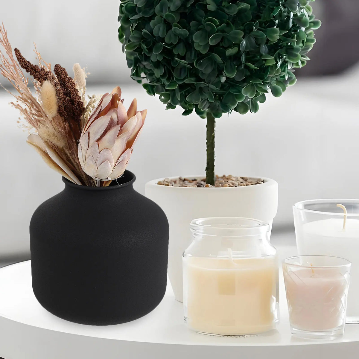 Vase en métal noir mat, style minimaliste Nesty, garni de fleurs séchées protéa et pampa, sur table avec bougies et plante en pot