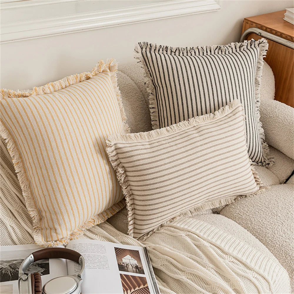 Housse de coussin en lin à rayures, plusieurs formats disponibles Nesty, trois housses de coussin à rayures (moutarde, noir et brun) avec bordures à franges, deux carrées et une rectangulaire, sur canapé écru