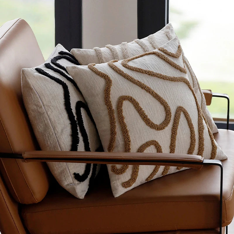 Housse de coussin en chénille tuftée, lignes simples Nesty, deux coussins en chénille écrue à motif tufté sinueux, l'un beige et l'un noir, calés sur fauteuil en cuir près d'une fenêtre