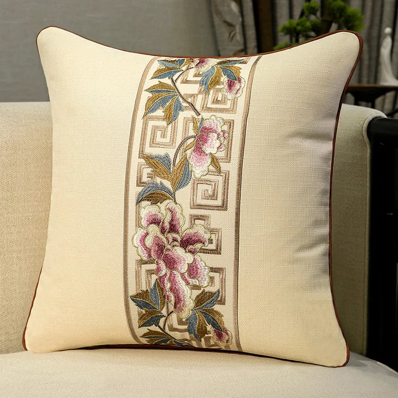 Housse de coussin en coton et lin, broderie florale classique Nesty, housse de coussin beige avec bande brodée de fleurs roses et motif grec doré, posée sur fauteuil