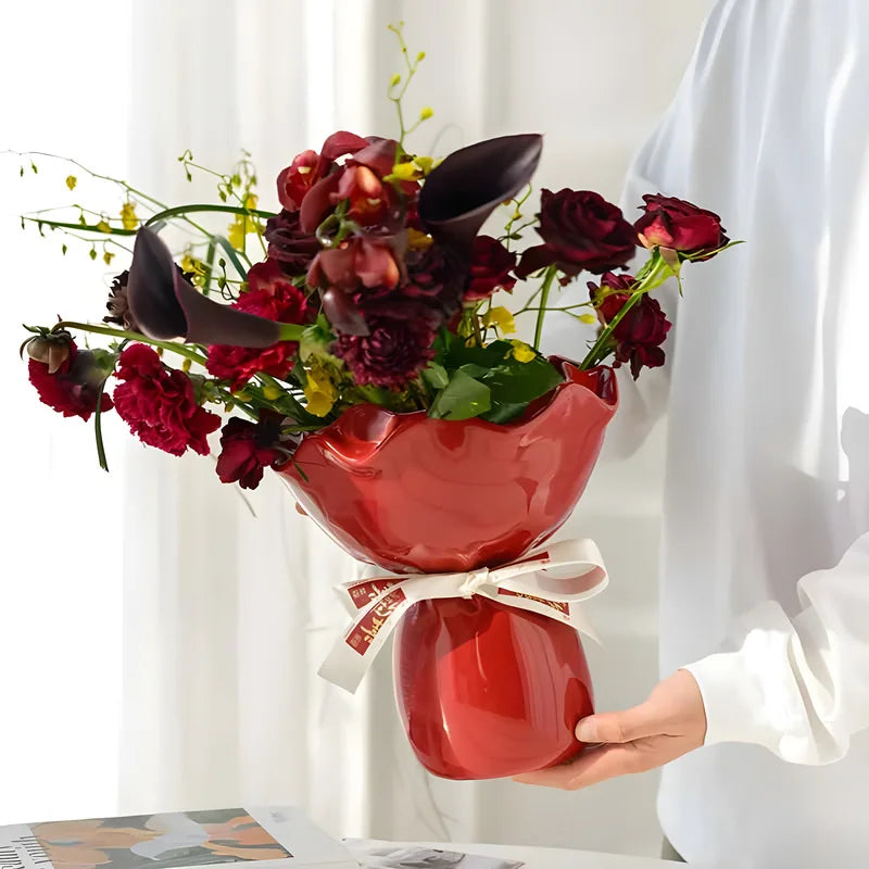 Vase en céramique en forme de rose, modèle bureau Nesty, vase céramique rouge à col ondulé garni d'un bouquet de fleurs sombres et rouges, tenu par une femme en blanc