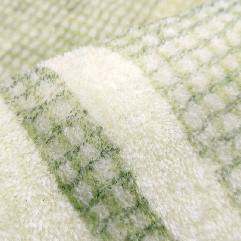 Gros plan sur la texture pelucheuse à motif de losanges verts et crème d'un tapis.