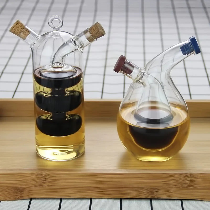 Flacon à sauce double compartiment en verre Nesty, deux flacons doseurs à deux compartiments remplis de sauce et d'huile, posés sur plateau en bambou, l'un à bouchons liège et l'autre à bouchons colorés