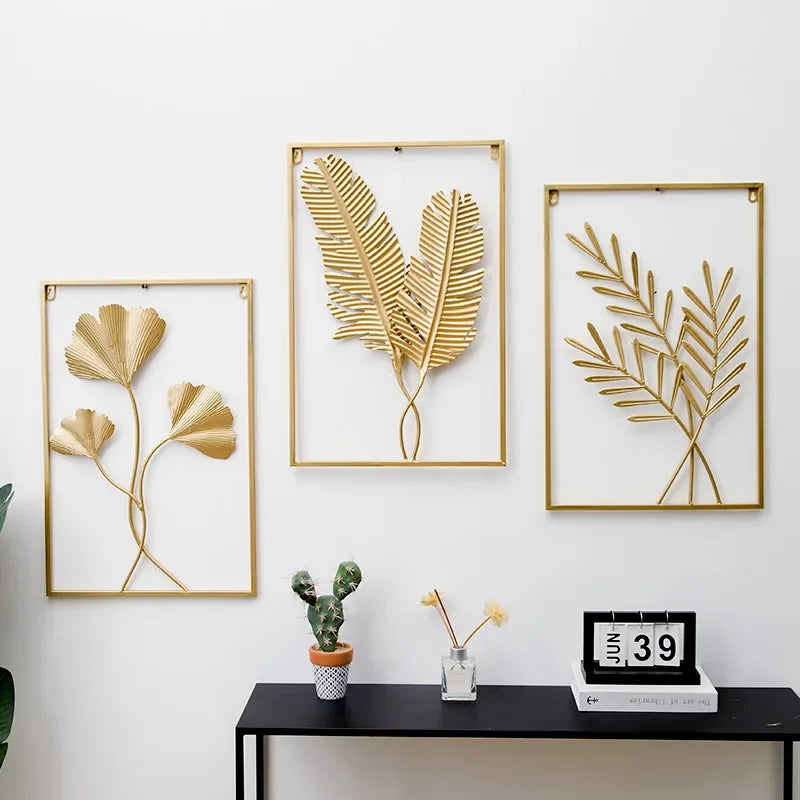 Pendentif mural en fer forgé à motif végétal Nesty, trois cadres dorés à motifs de feuilles de gingko, de fougère et de palme sur un mur blanc, au-dessus d'une console noire