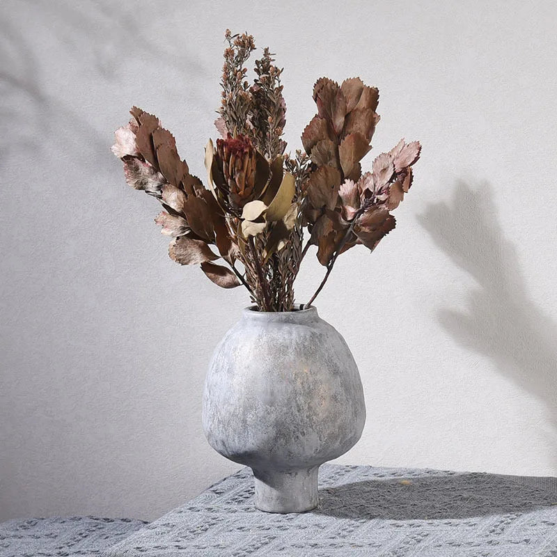 Vase en poterie fait main, grain brut, esprit artisanal Nesty, vase gris texturé en forme de galet sur pied, garni de feuillage séché brun et rose, fond blanc