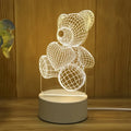 Veilleuse LED ours en acrylique Nesty - Allumée sur une table en bois, fleur à côté
