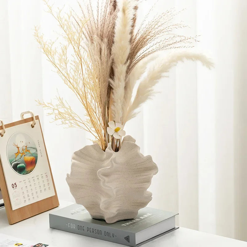 Vase en céramique à motifs ondulés, forme pétale Nesty, vase garni de graminées séchées et d'une fleur blanche, posé sur un livre