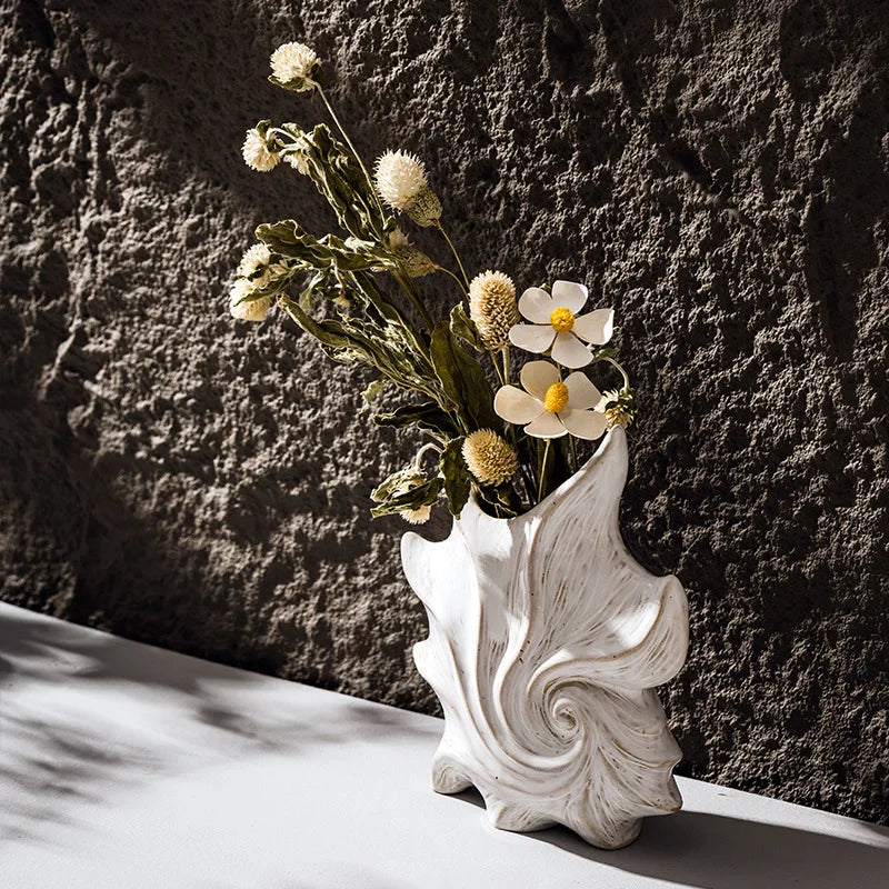 Vase en céramique blanche forme coquillage Nesty - Vue en angle avec fleurs séchées, sur surface blanche devant mur en pierre