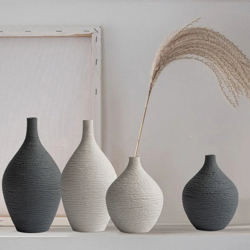Vase en céramique à col étroit, style nordique sobre Nesty, quatre vases en céramique texturée forme bouteille de tailles et coloris différents (anthracite, blanc cassé, gris clair), alignés devant un cadre