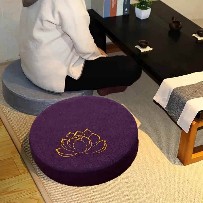 Coussin de méditation en lin, texture lotus, modèle compact Nesty, coussin rond violet brodé d'un lotus doré sur tatami, personne assise en tailleur sur un coussin gris devant une table basse noire avec service à thé