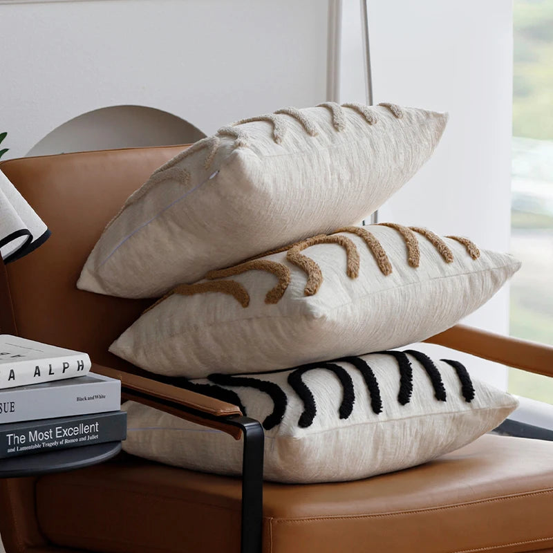 Housse de coussin en chénille tuftée, lignes simples Nesty, trois coussins en chénille écrue empilés, motifs tuftés en lignes sinueuses beige et noir, sur fauteuil en cuir cognac
