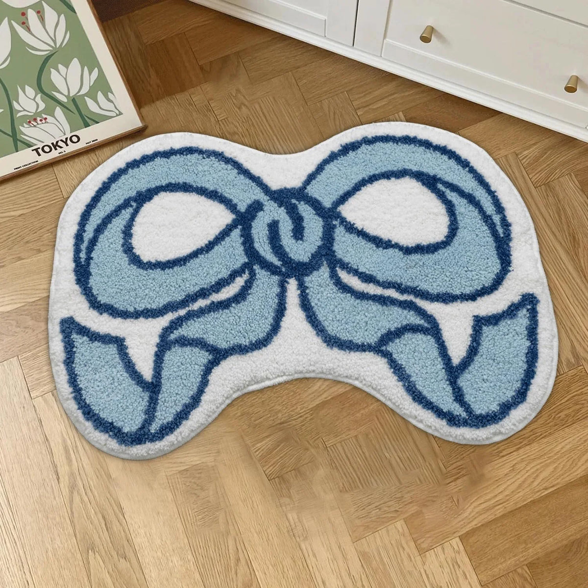 Petit tapis à motif nœud — imitation cachemire - Nesty, variante bleu et blanc posée sur un parquet devant une commode blanche