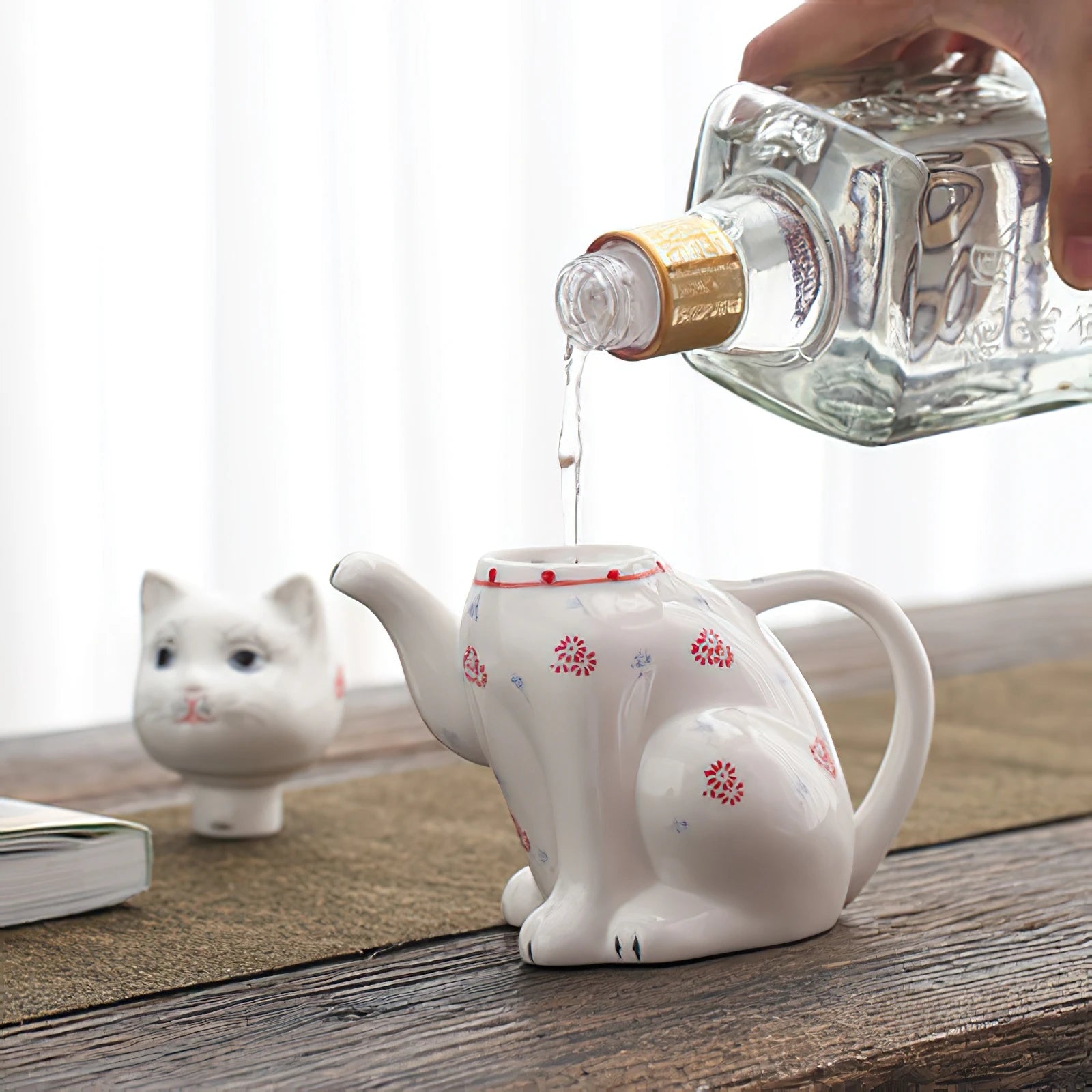 Théière en porcelaine forme de chat Nesty, eau versée depuis une carafe dans l'ouverture au niveau du cou, tête posée à côté