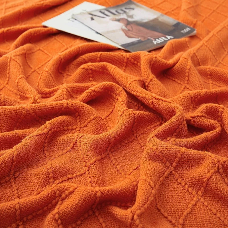 Plaid oversize tricoté moelleux Nesty - Coloris orange froissé, gros plan sur le motif losanges avec un magazine posé dessus