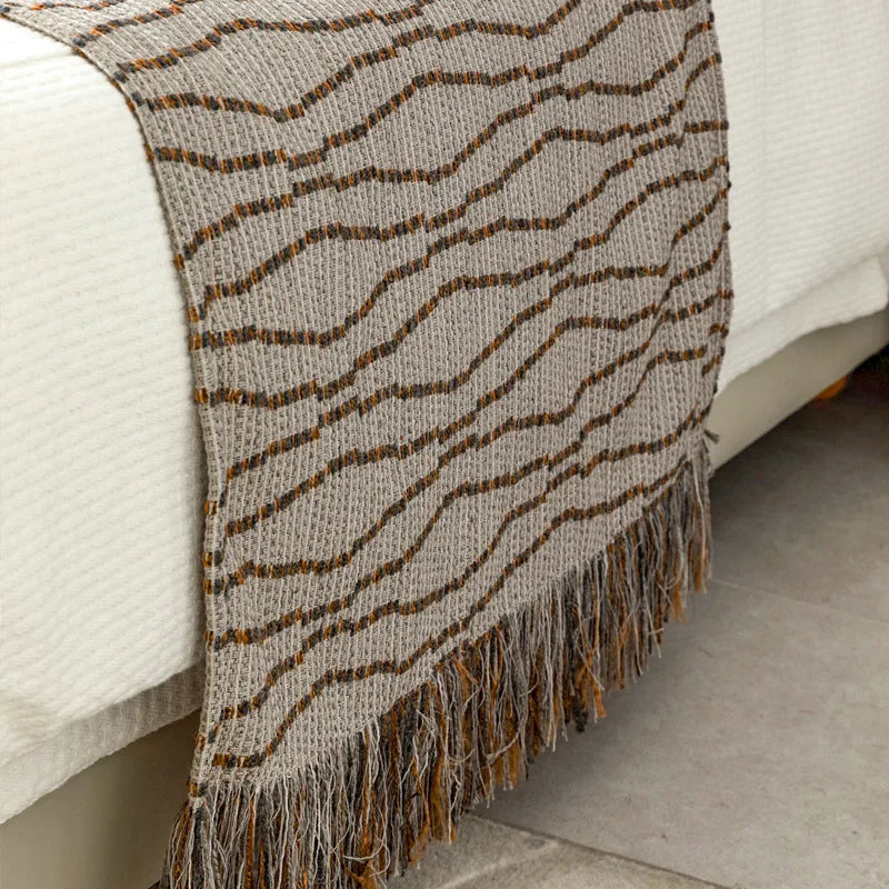 Housse de coussin en coton et lin beige, bordure texturée Nesty, gros plan sur le chemin de lit à motif de lignes ondulées brunes et oranges avec frange, posé sur lit blanc