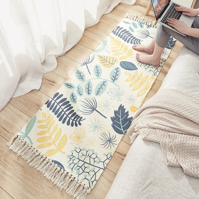 Tapis en coton et lin tissé main — motif berbère - Nesty, variante motif feuilles et fleurs bleues et jaunes, personne assise avec un ordinateur portable à proximité