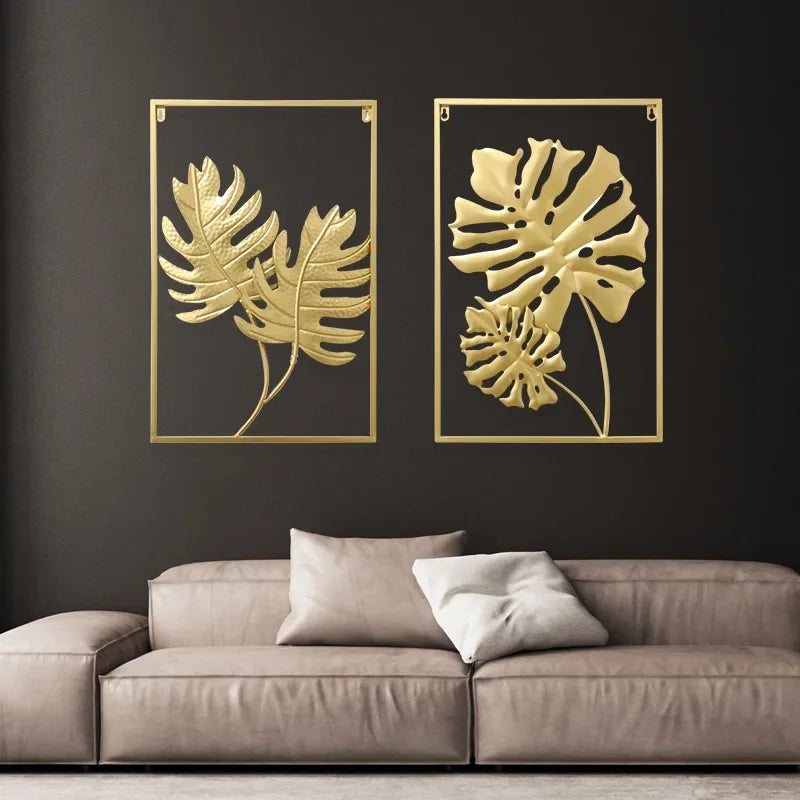 Pendentif mural en fer forgé à motif végétal Nesty, deux cadres dorés à motifs de fougère et de monstera sur un mur noir, au-dessus d'un canapé beige