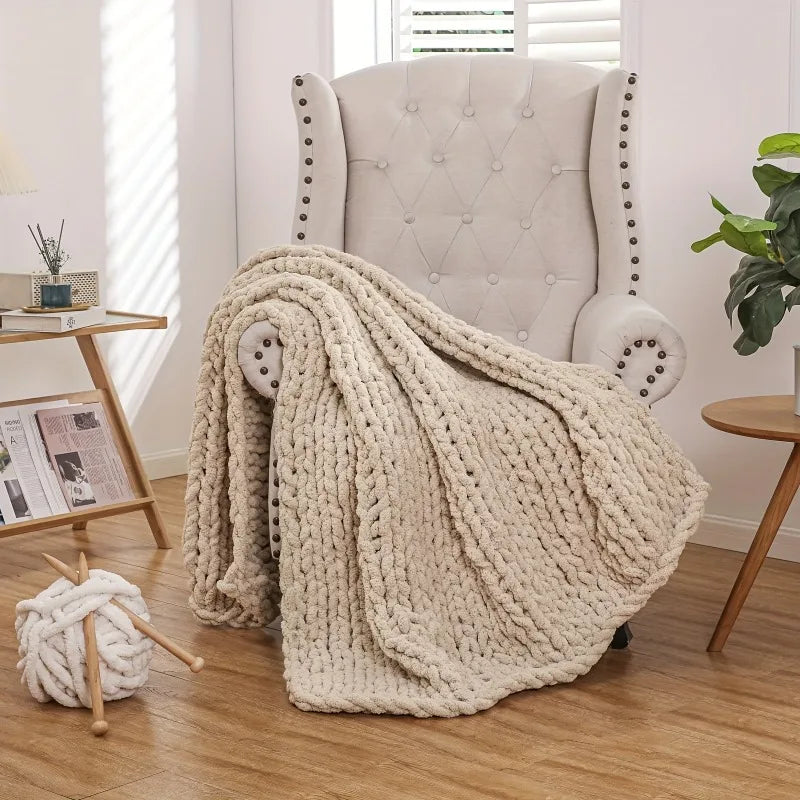 Plaid tricoté chunky knit Nesty - Drapé sur fauteuil capitonné clouté, avec pélote de laine et aiguilles au sol
