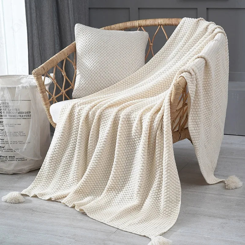 Plaid tricoté uni gaufré Nesty - Coloris blanc cassé drapé sur fauteuil en rotin, franges effilées