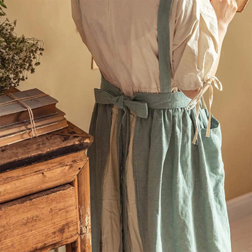 Détail de dos du tablier en coton et lin vert sauge, nœud à la taille et poche, devant un meuble en bois ancien - Nesty