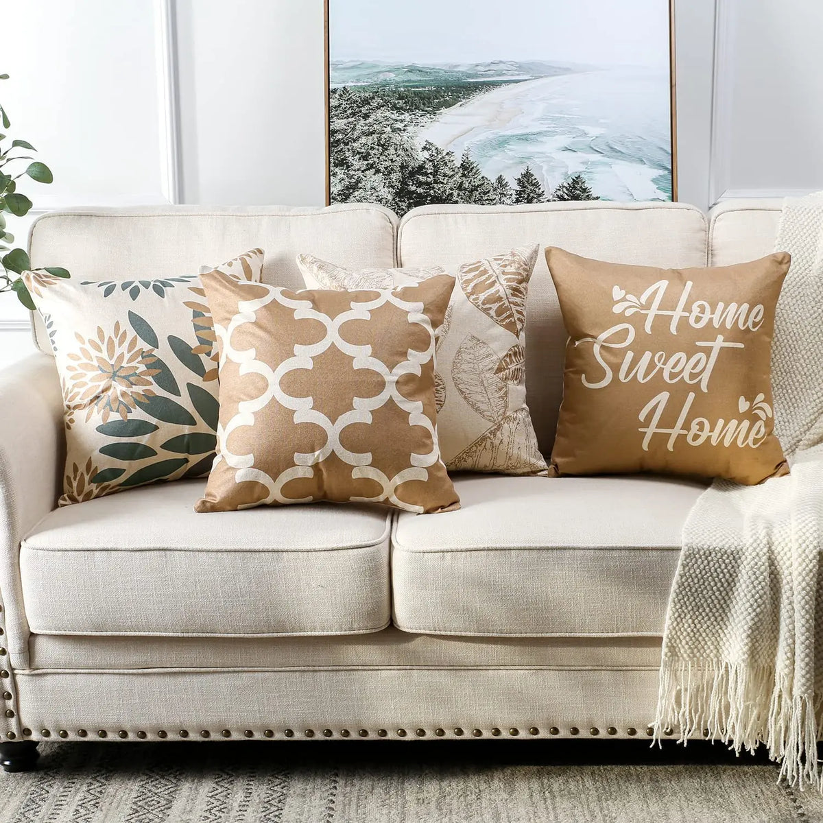 Housse de coussin en lin, motif feuille géométrique brun clair, modèle 2 Nesty, cinq housses de coussin beige et taupe alignées sur canapé clair (quadrillage doré, "Home Sweet Home", feuilles XL, fleurs bicolores)