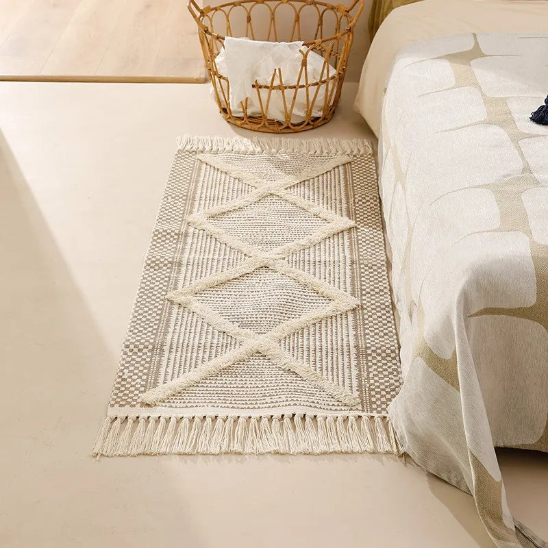 Tapis noué main à franges — motif géométrique - Nesty, tapis tissé écru à motif losange en relief, franges aux extrémités, posé au pied d'un lit près d'un panier en osier