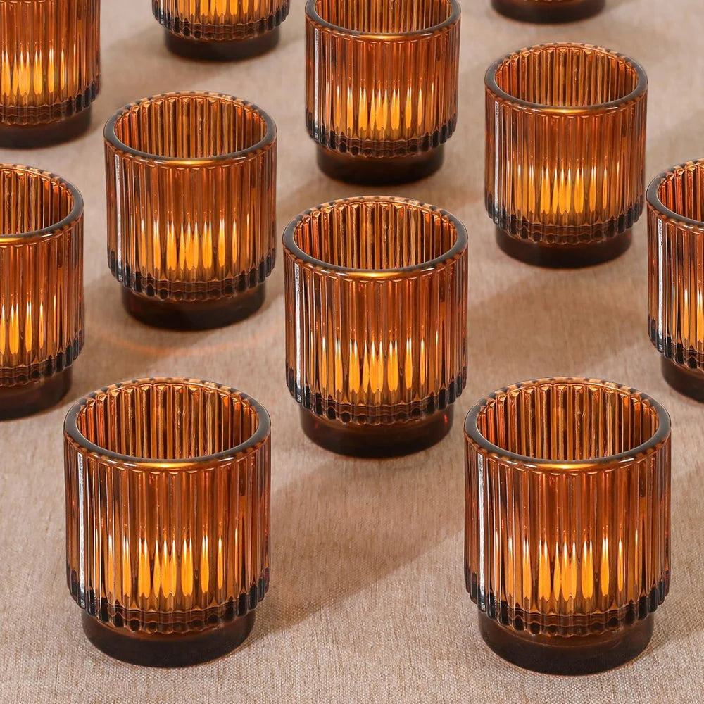 Photophores en verre ambré Nesty - Plusieurs photophores côtelés ambrés allumés, disposés en quinconce sur un tissu beige