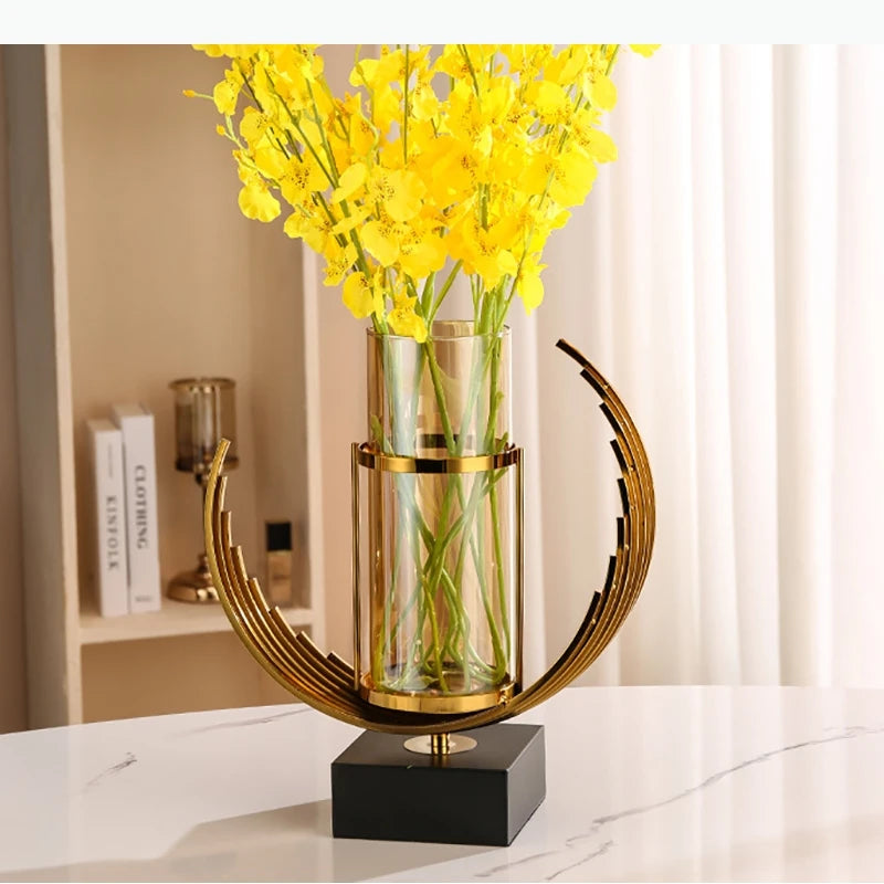 Vase en verre à base dorée Nesty - Avec orchidées jaunes, sur table en marbre blanc près d'une bibliothèque