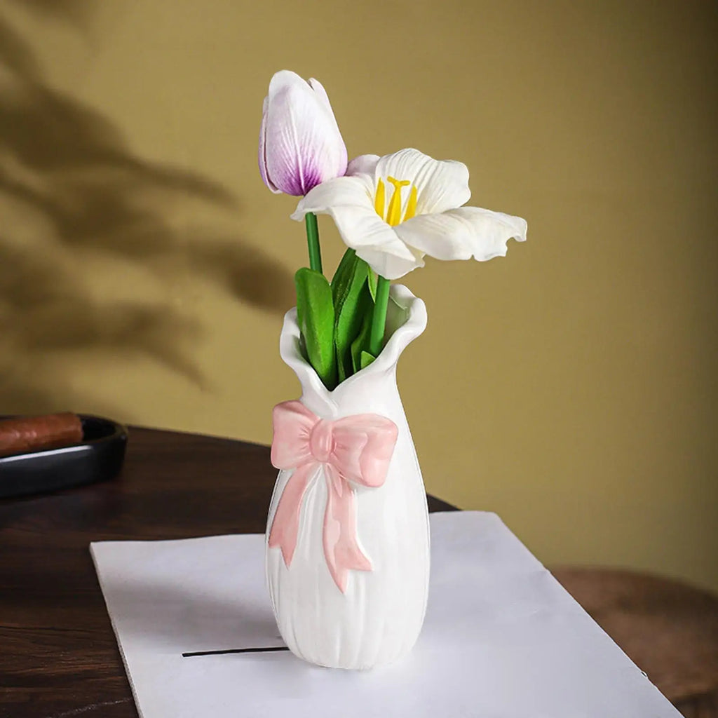 Vase en céramique avec détail nœud, décoration étagère Nesty, gros plan sur le vase à col ondulé et nœud rose, garni d'une tulipe mauve et d'une fleur blanche, posé sur papier