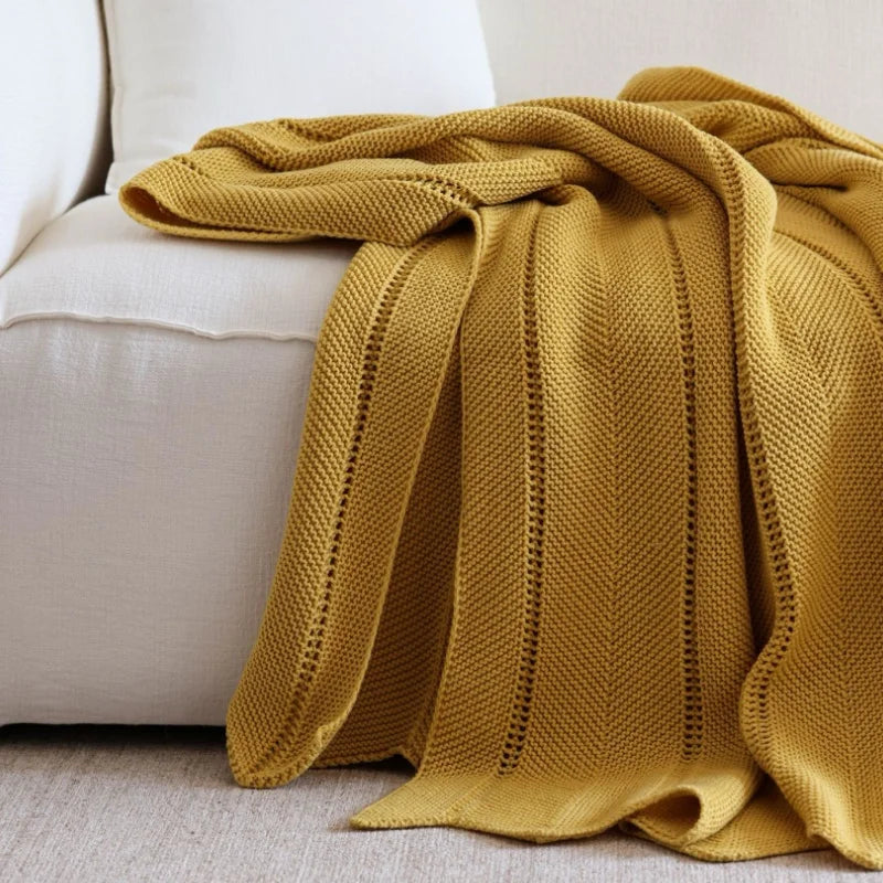 Plaid tricoté en acrylique coloris jaune moutarde, drapé sur l'accoudoir d'un canapé beige, gros plan sur les mailles - Nesty
