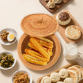 Panier de rangement artisanal en rotin naturel avec couvercle Nesty, panier ouvert garni de beignets de pâte frite, entouré de petits plats de petit-déjeuner asiatique