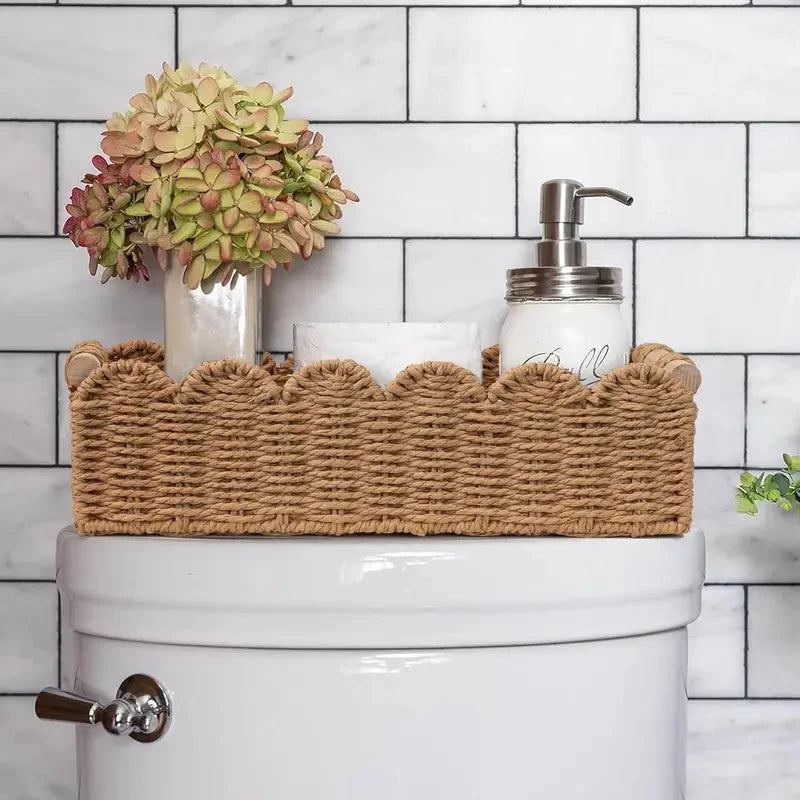 Panier de rangement en corde de papier tressée, bord festonné et poignées en bois Nesty, panier posé sur un réservoir de toilettes avec vase d'hortensias séchés et distributeur de savon, salle de bain carrelée