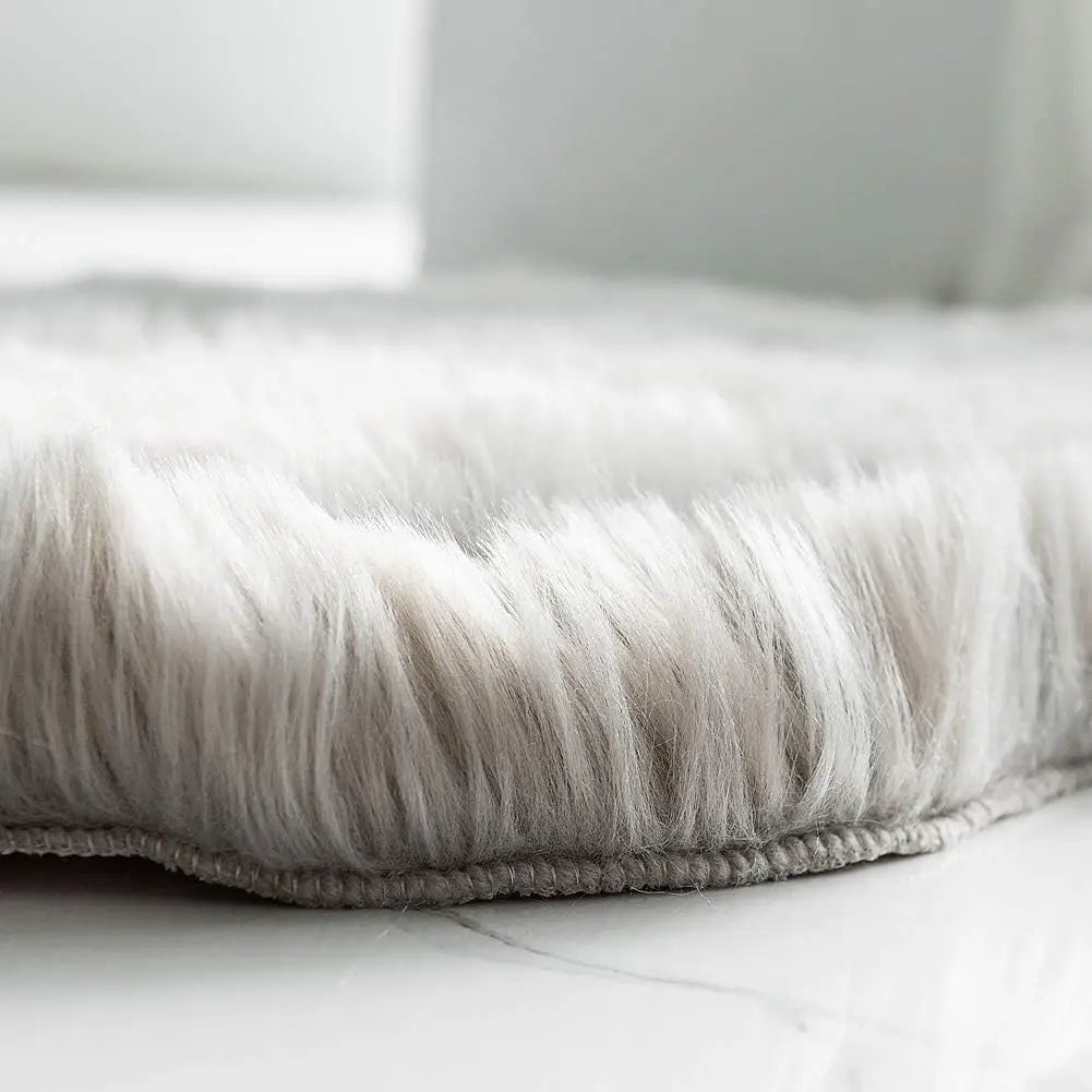 Gros plan sur le bord d'un tapis en fausse fourrure blanche et grise, montrant la longueur du poil et la bordure cousue.