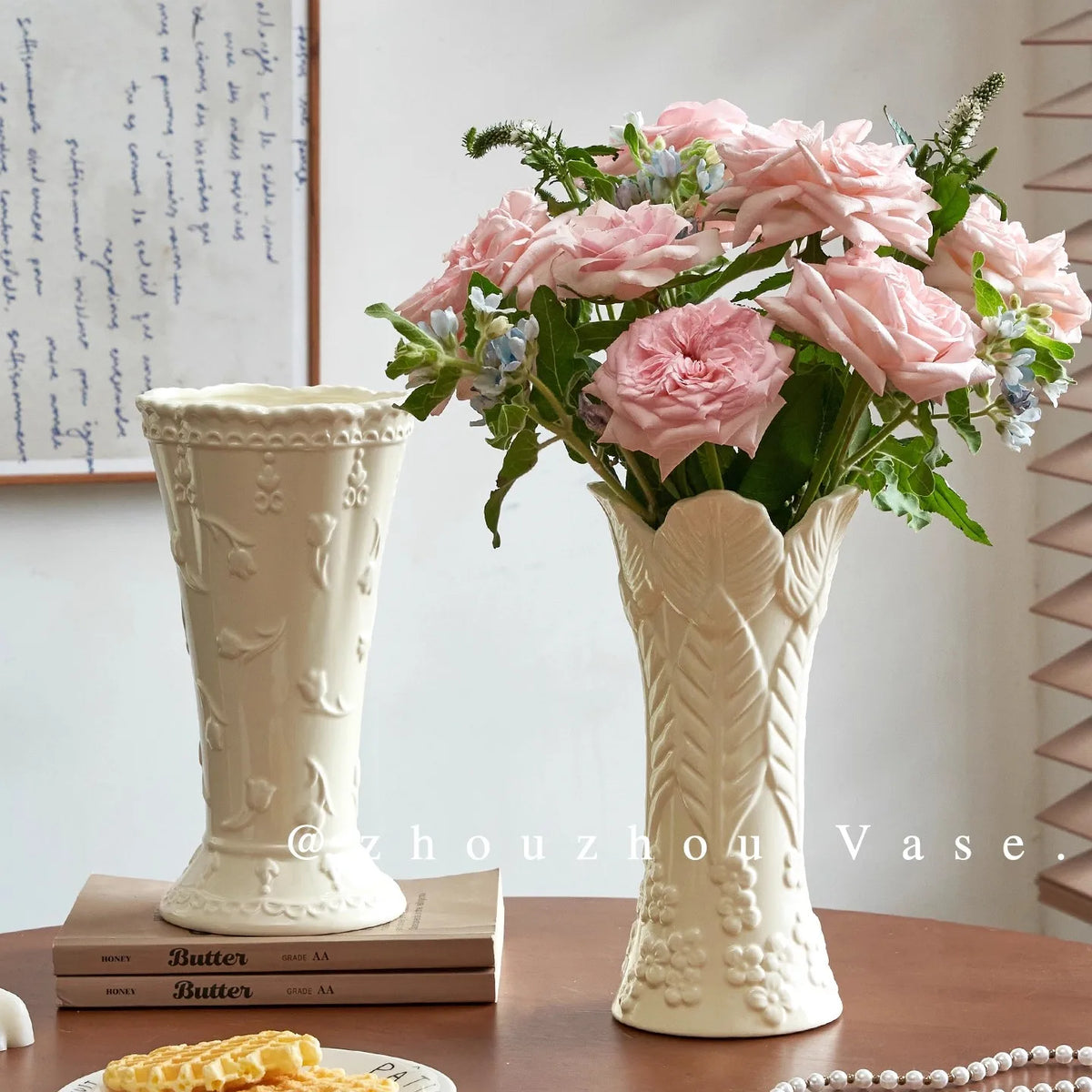 Vase en céramique crème à relief, style intemporel Nesty, deux vases à relief floral et à feuilles gaufrées, l'un garni de roses roses, sur une table en bois