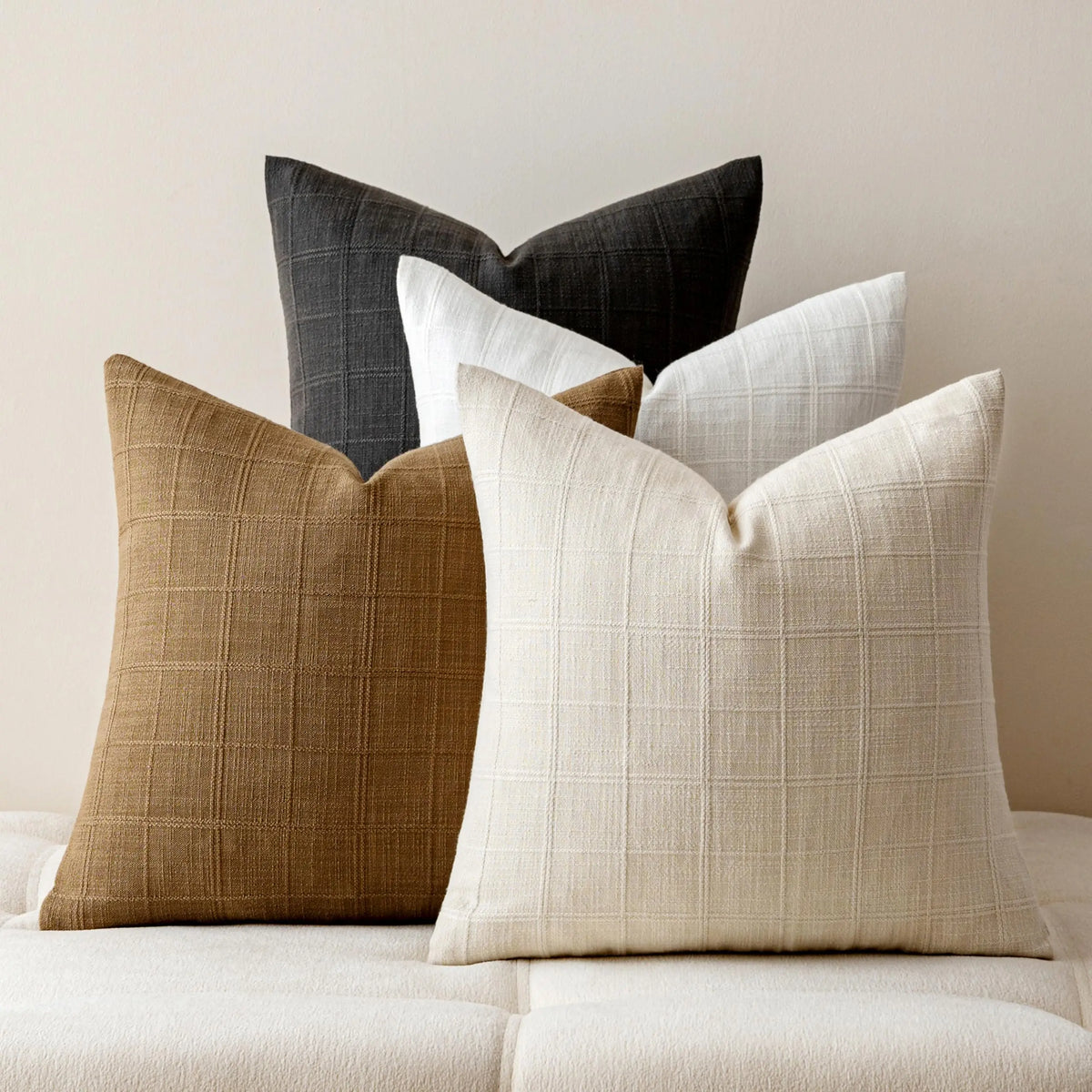 Housse de coussin en lin à carreaux, esprit campagne Nesty, quatre housses de coussin en lin à motif carreaux tissé, coloris anthracite, camel, écru et beige, empilées sur canapé clair