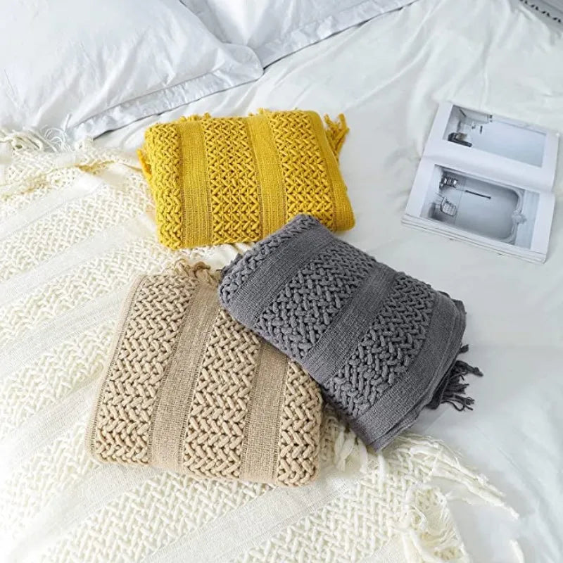 Plaid tricoté texture jacquard Nesty - Trois coloris jaune moutarde, beige et gris pliés sur lit, près d'un magazine