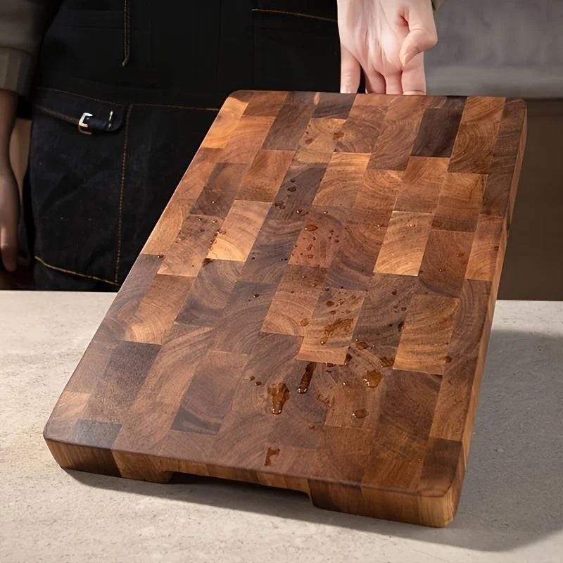 Grande planche à découper en bois massif à grain apparent Nesty, planche tenue inclinée en main avec des gouttes d'huile sur la surface, personne en tablier