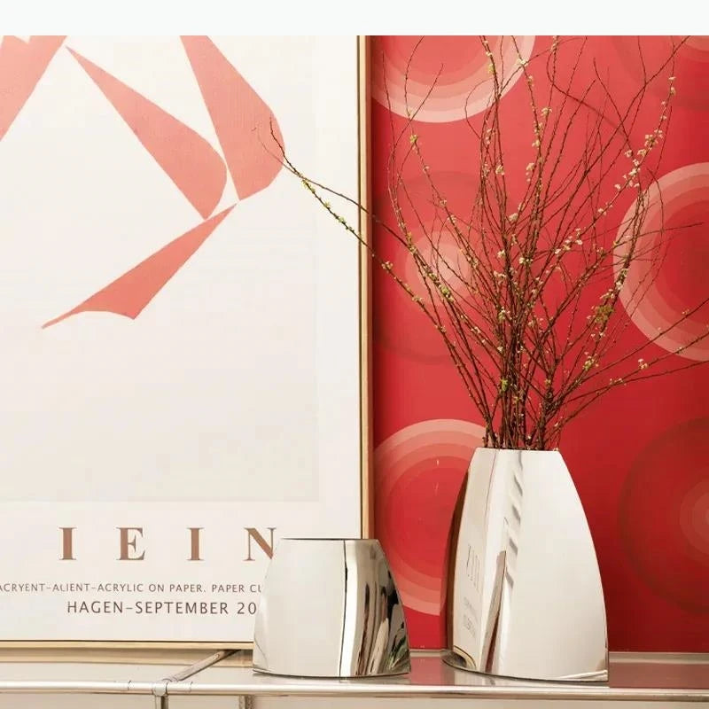 Vase arc en métal argenté — silhouette minimaliste - Nesty - Deux tailles avec branches fleuries, devant une affiche murale rouge et un cadre