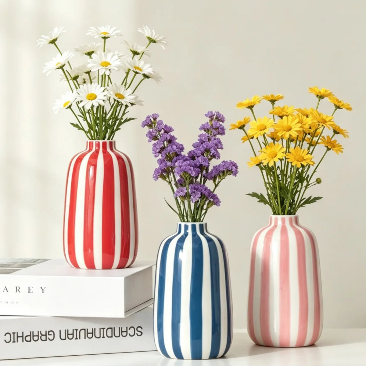 Vase en céramique à rayures géométriques Nesty - Trois coloris (rouge, bleu, rose) avec fleurs des champs, sur étagère avec livres