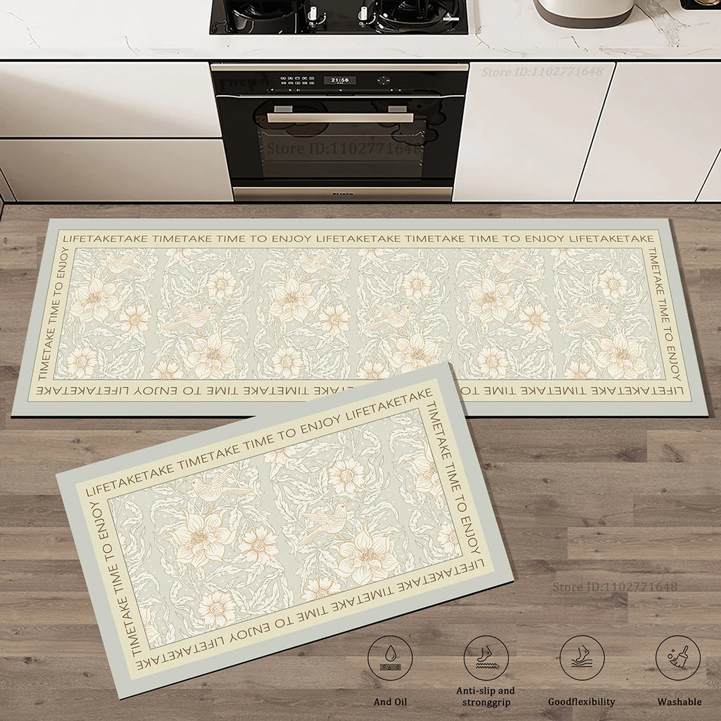 Set de deux tapis de cuisine à motif floral et d'oiseaux sur fond vert sauge avec bordure à inscription, posés devant une cuisinière.