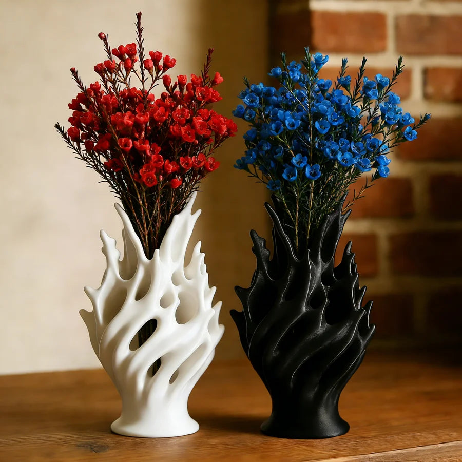 Vase en plastique léger, format table à manger Nesty, formes ajourées en flamme, blanc et noir, garnies de fleurs rouges et bleues, devant un mur en briques