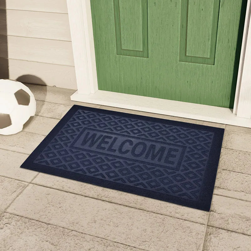 Paillasson en caoutchouc bleu marine motif losanges gravé 'Welcome', posé devant une porte d'entrée verte - Nesty