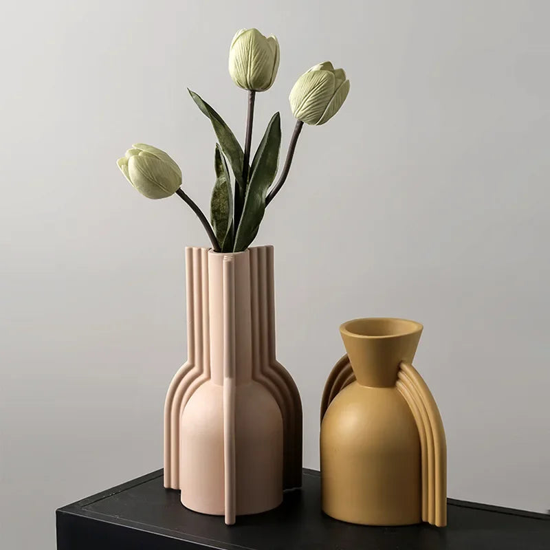 Vase en céramique, forme géométrique irrégulière nordique Nesty, vase rose pâle à cannelures garni de tulipes vertes, à côté d'un vase jaune moutarde vide, sur meuble noir
