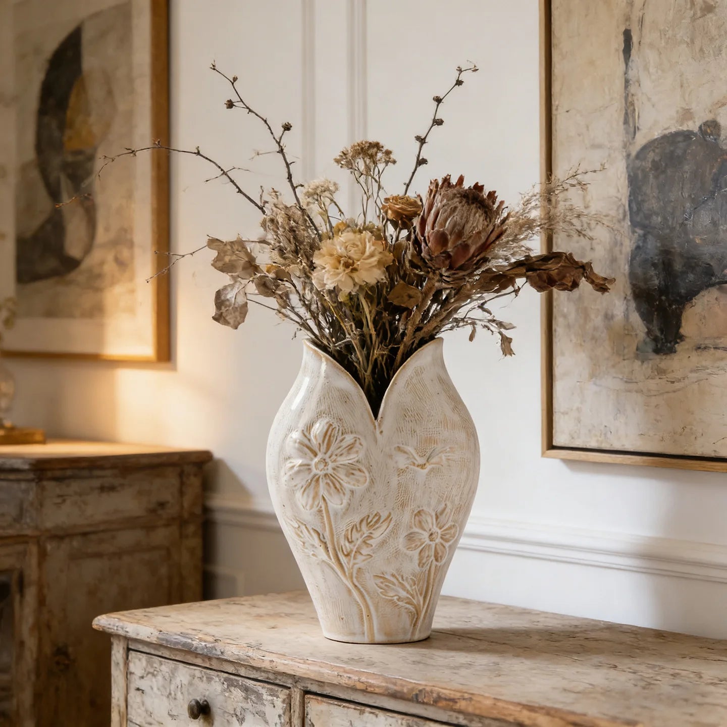 Vase en céramique forme poisson, esprit wabi-sabi Nesty, vase blanc à relief floral, garni d'un bouquet de branches et fleurs séchées, entre deux tableaux anciens