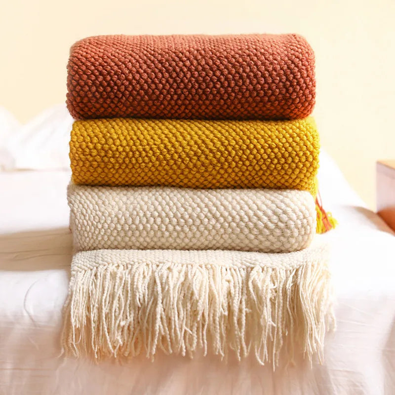 Plaid en maille chunky à franges, tricot épais pour canapé Nesty, quatre plaids en maille chunky empilés à franges, coloris terracotta, moutarde et écru, posés sur lit blanc